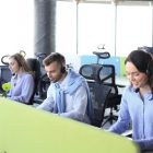 Young employee working with a headset and accompanied by her team